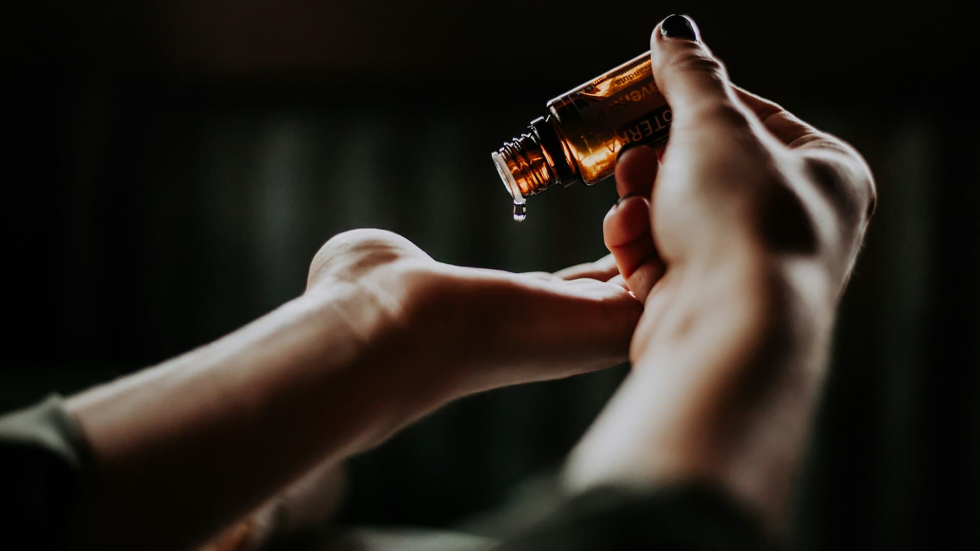 Tangan menggenggam botol kaca amber berisi minyak herbal, tradisi perawatan ala Ayurveda