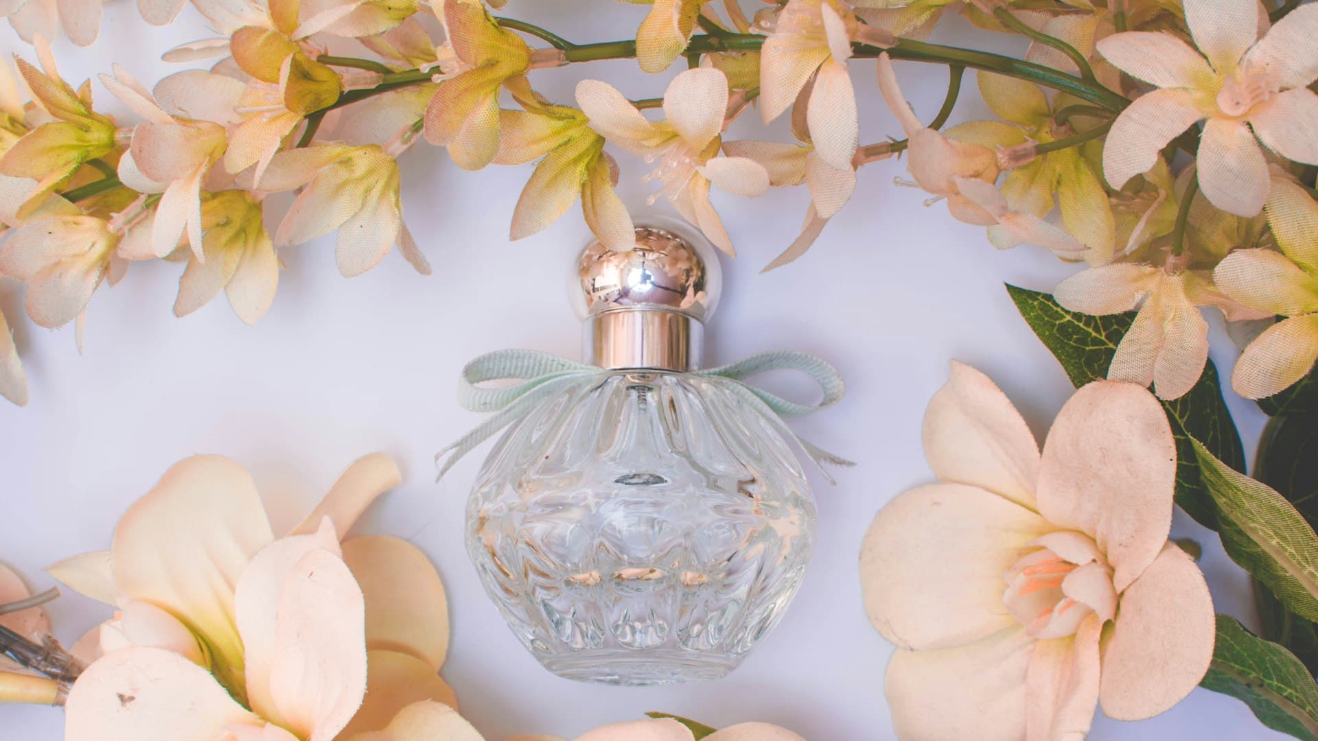 Botol parfum kaca bening berdampingan dengan kuntum bunga putih yang harum