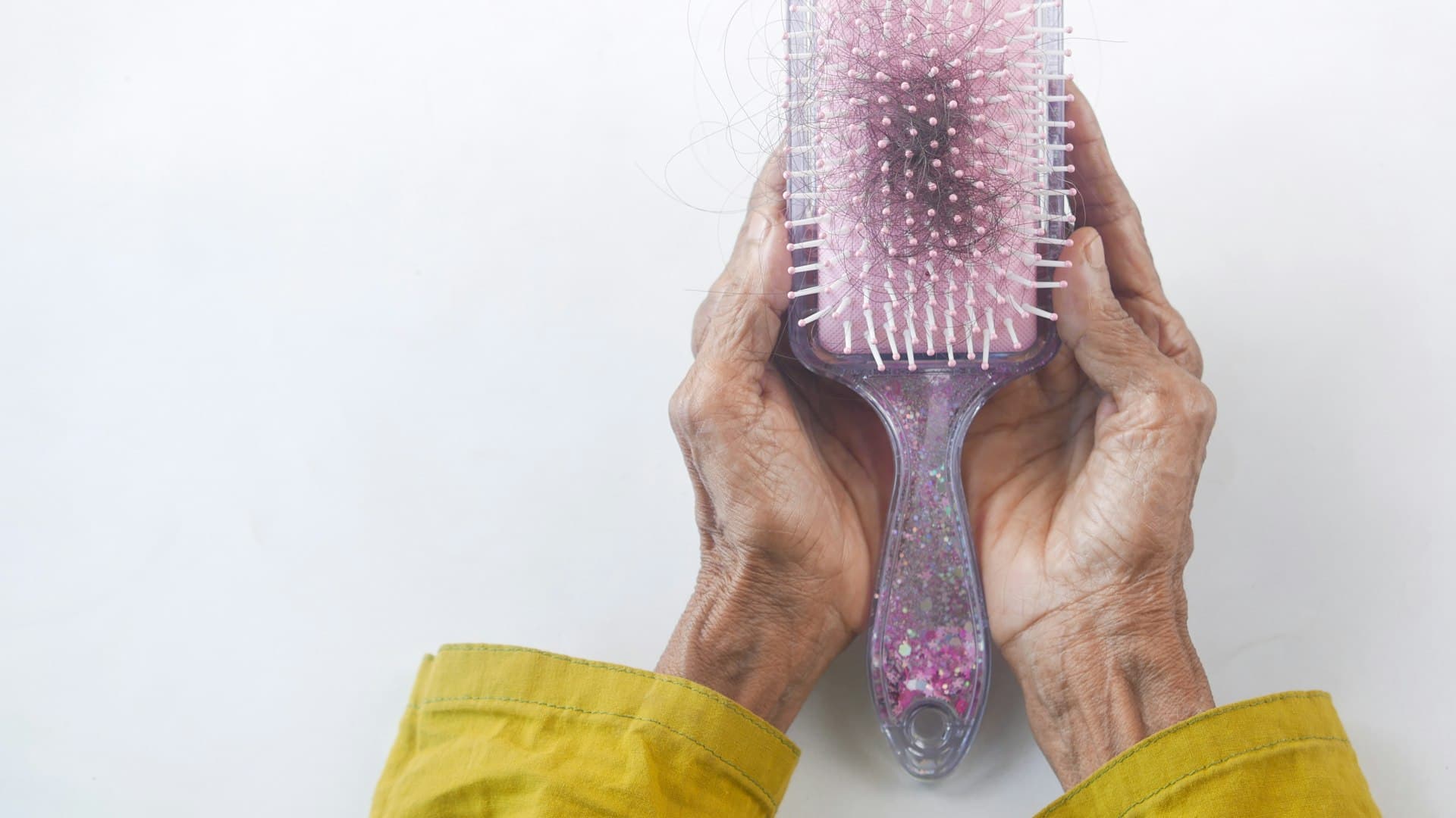 Sepasang tangan memegang sikat rambut dengan helai-helai yang tersangkut, momen jujur menghadapi kerontokan