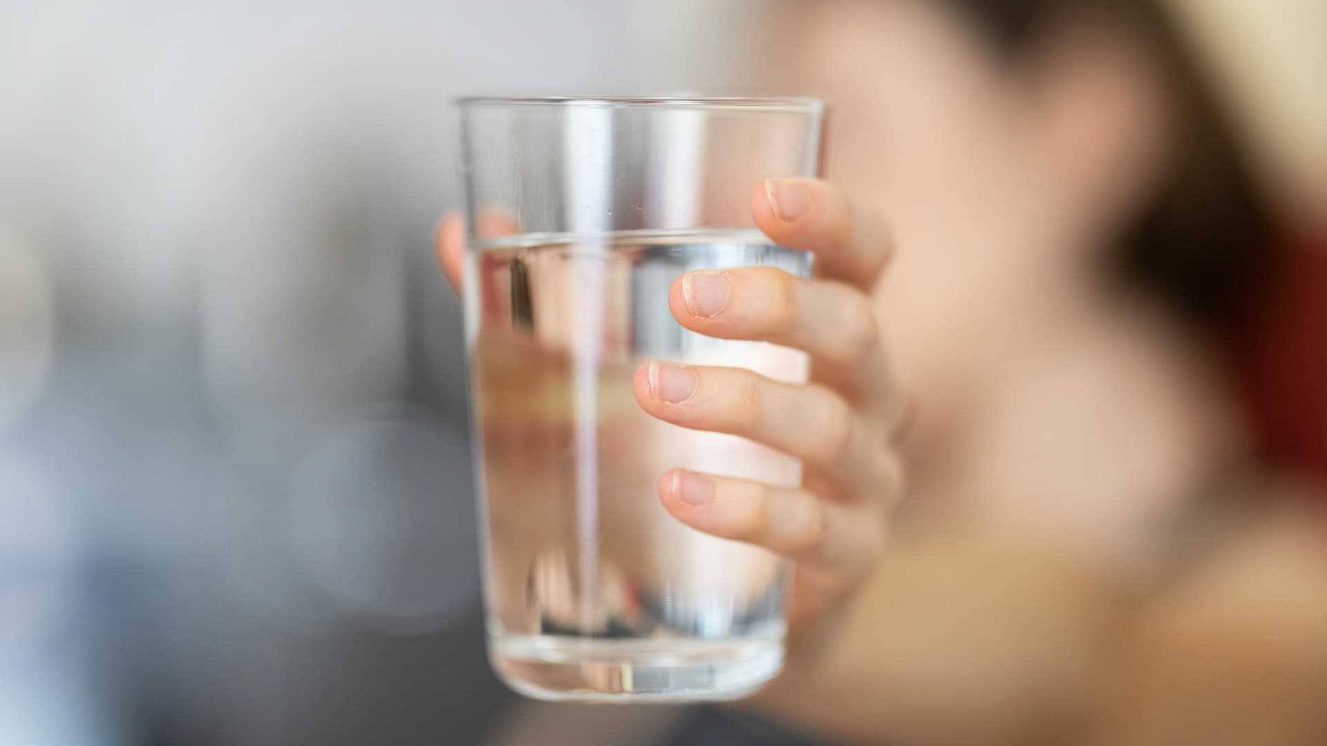 Tangan menggenggam gelas bening berisi air, ritual sederhana sebelum mengonsumsi suplemen