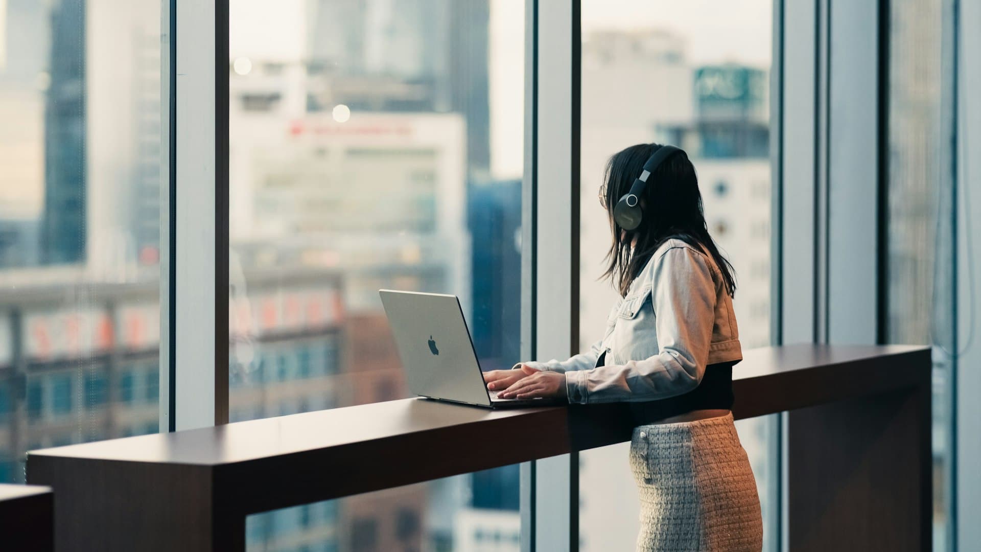 Perempuan mengenakan headphone bekerja dengan laptop di dekat jendela, menandai babak karier baru