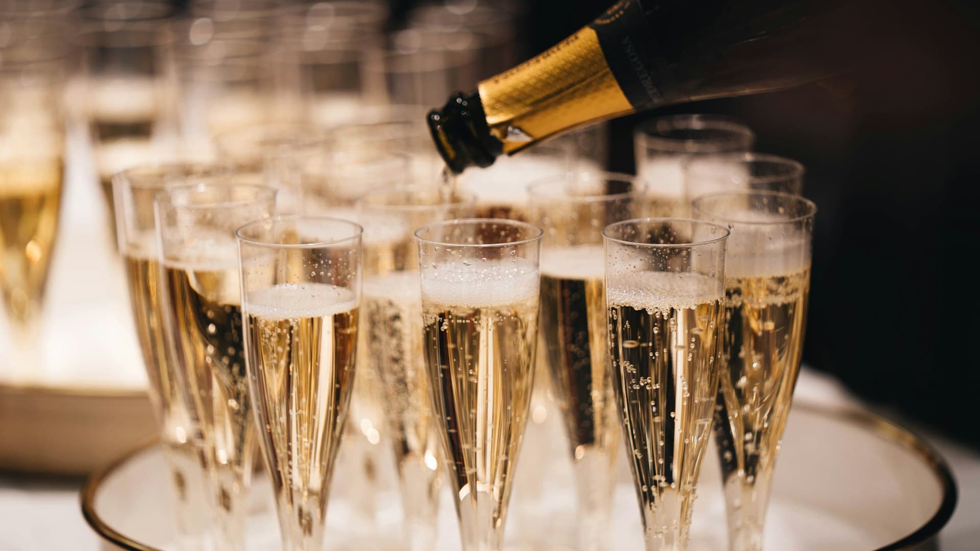 Para perempuan bergaun elegan berbincang sambil memegang gelas champagne di acara gala