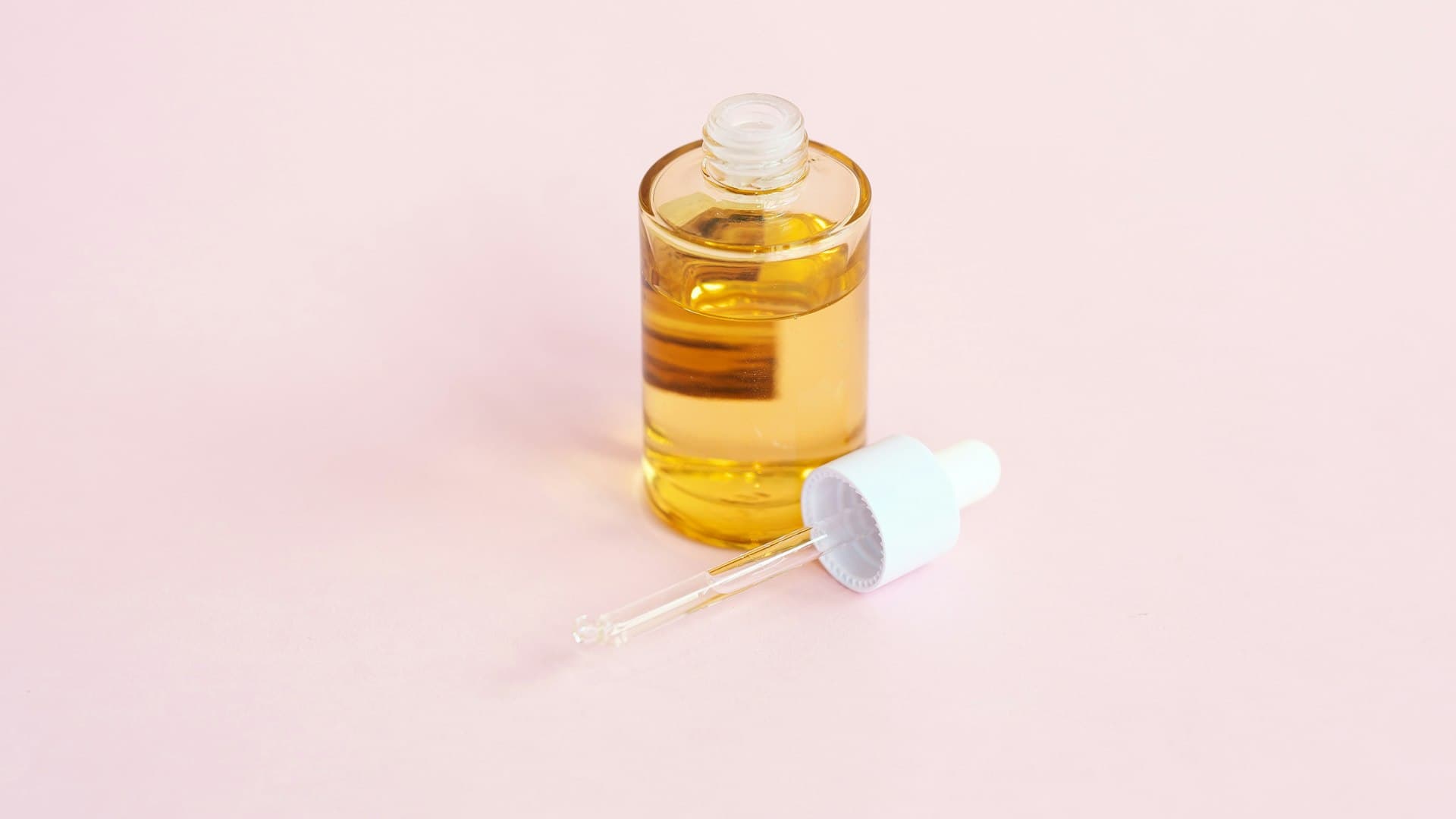 Botol serum perawatan kulit dengan pipet di atas permukaan berwarna merah muda lembut
