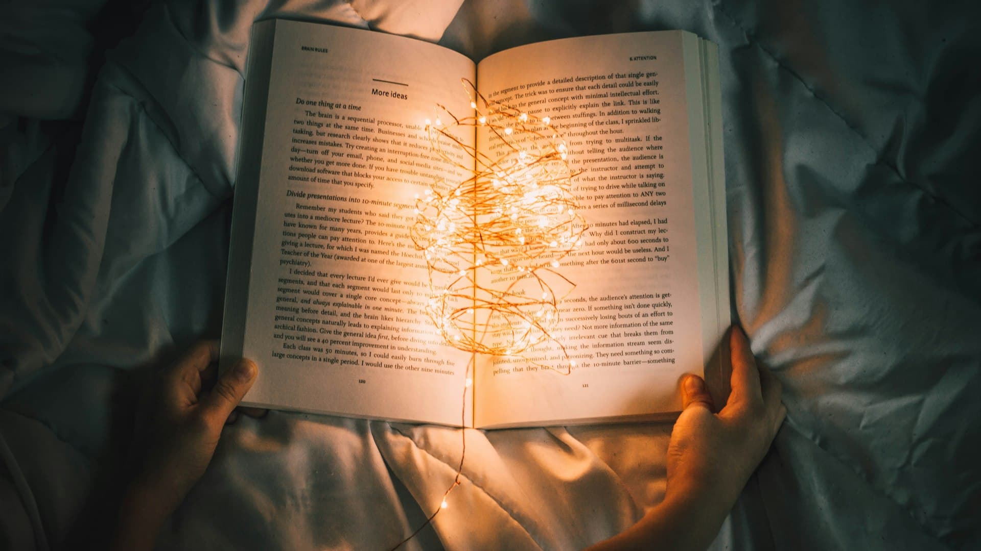 Tangan memegang untaian lampu kecil di atas buku yang terbuka, menandai halaman terakhir