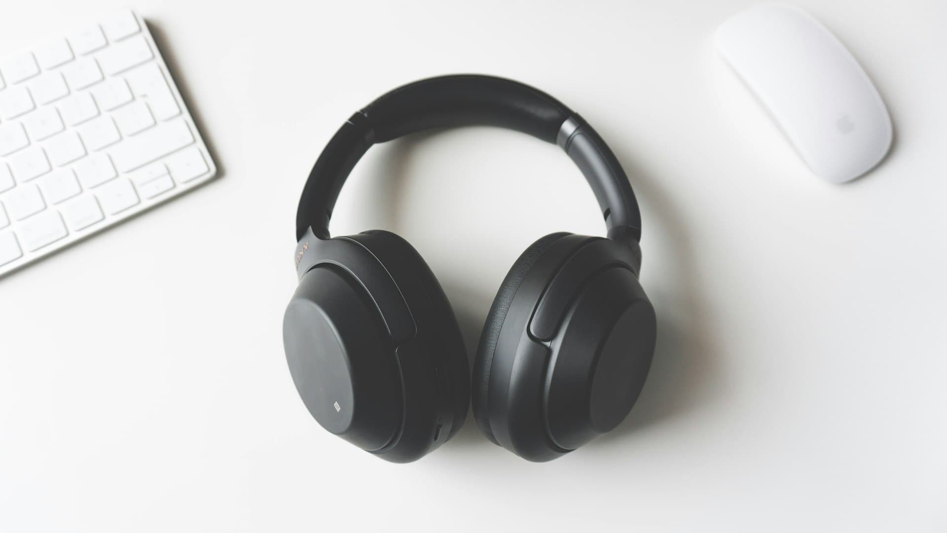 Headphone nirkabel hitam tergeletak di meja kerja putih, jeda meditasi di tengah hari sibuk
