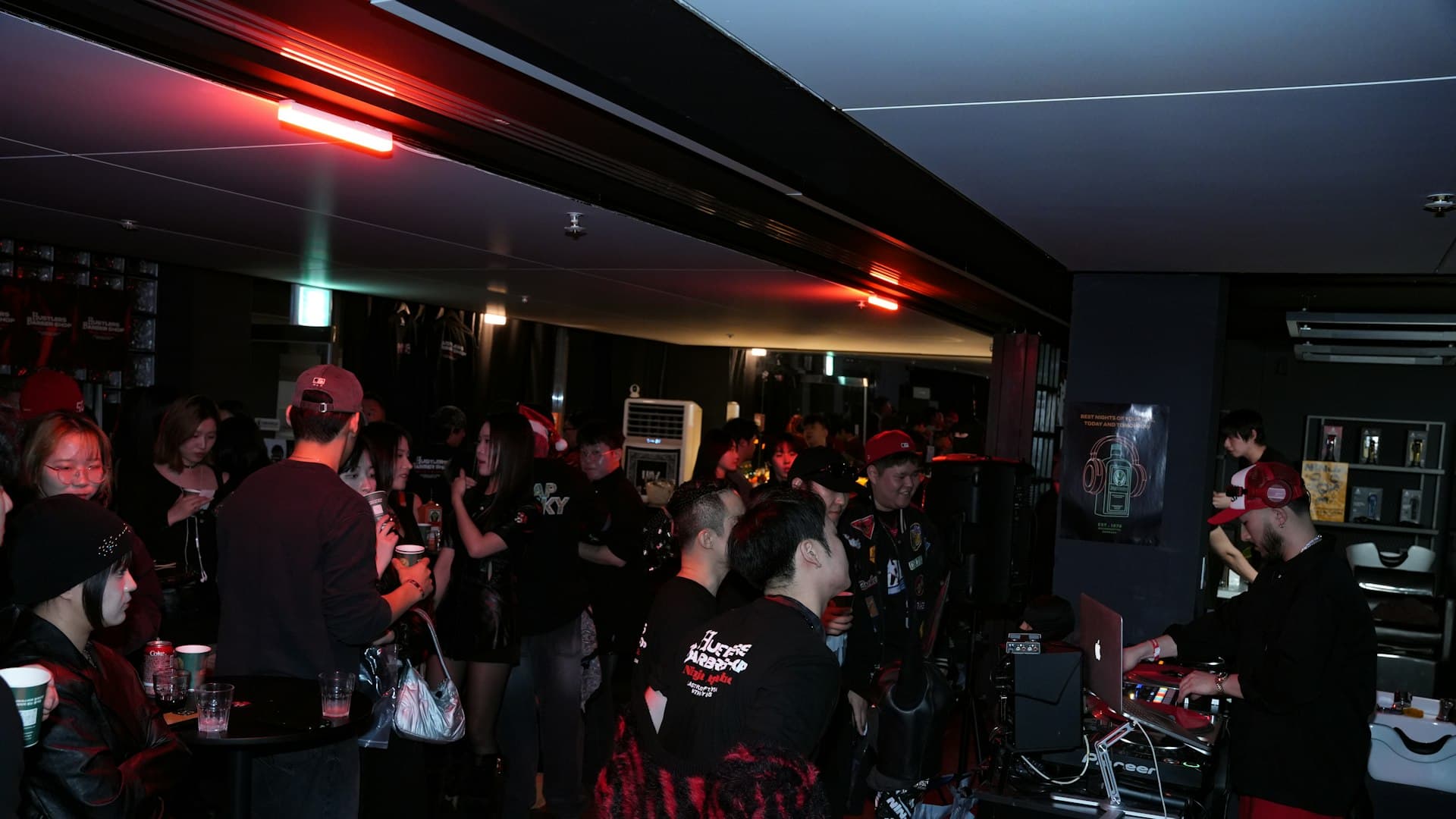 Seorang DJ memainkan musik di hadapan kerumunan yang larut dalam suasana, energi khas malam komunitas urban
