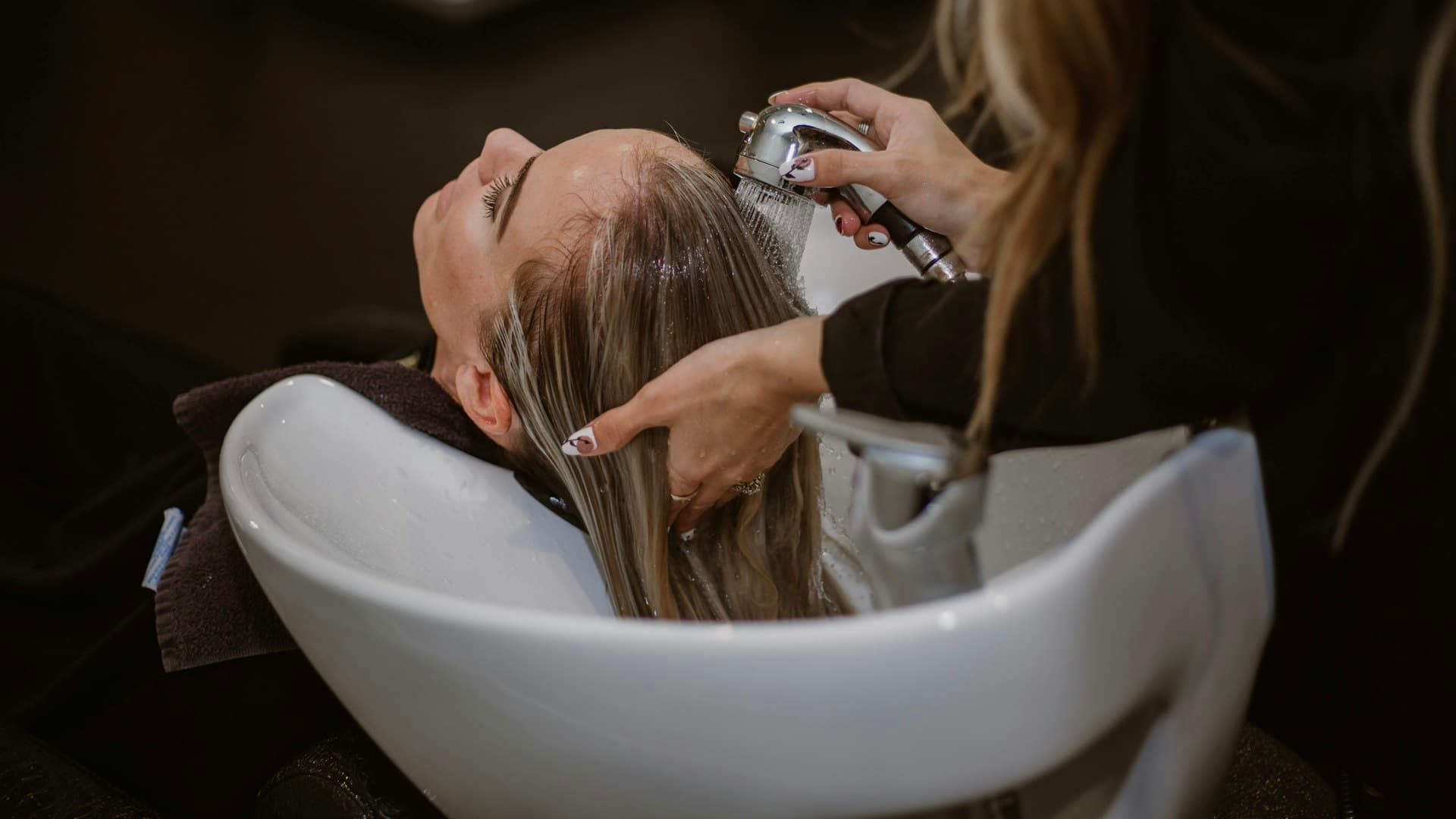 Seorang perempuan menerima perawatan rambut dan kulit kepala dari hairstylist di salon