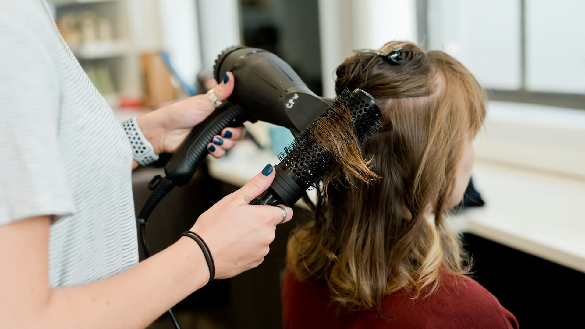 Perempuan berkemeja merah lengan panjang memegang hair dryer, bersiap menata potongan bob-nya