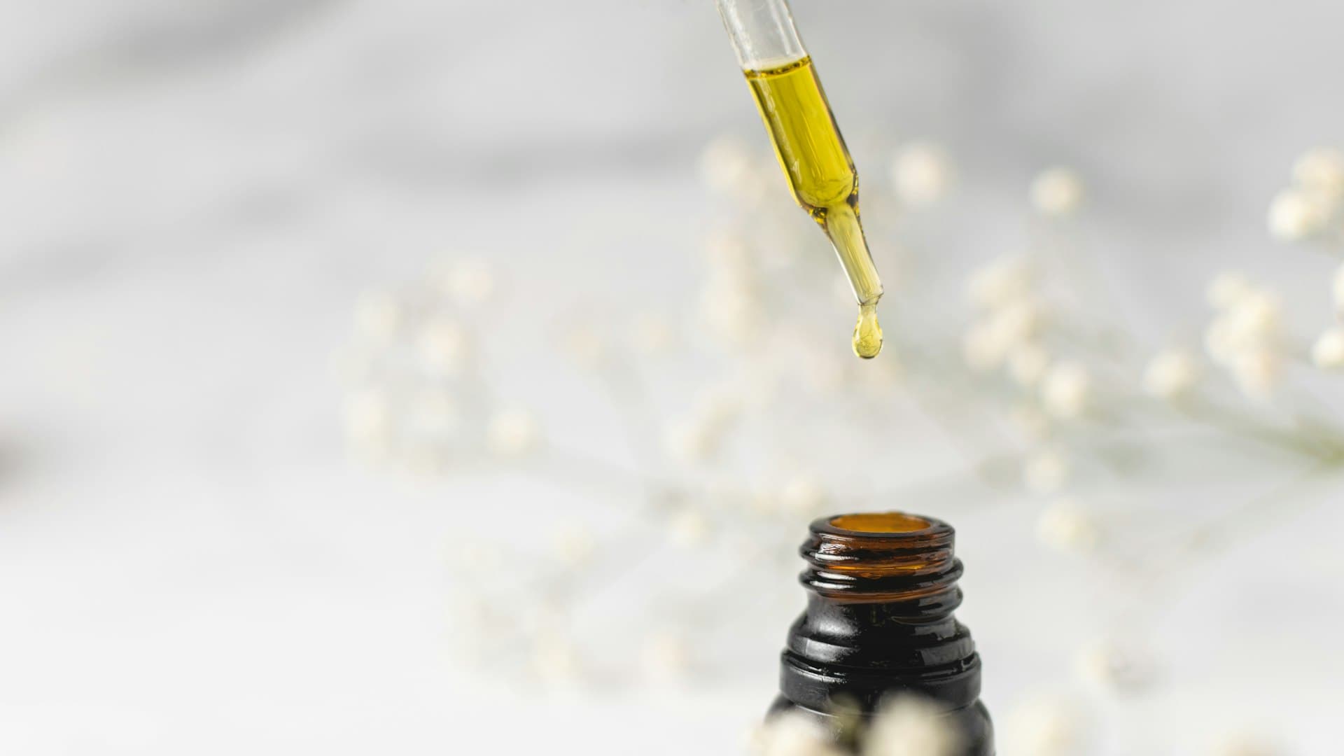 Botol kaca bening berisi minyak wajah dengan tutup berwarna kuning, ditata bersih dan minimalis