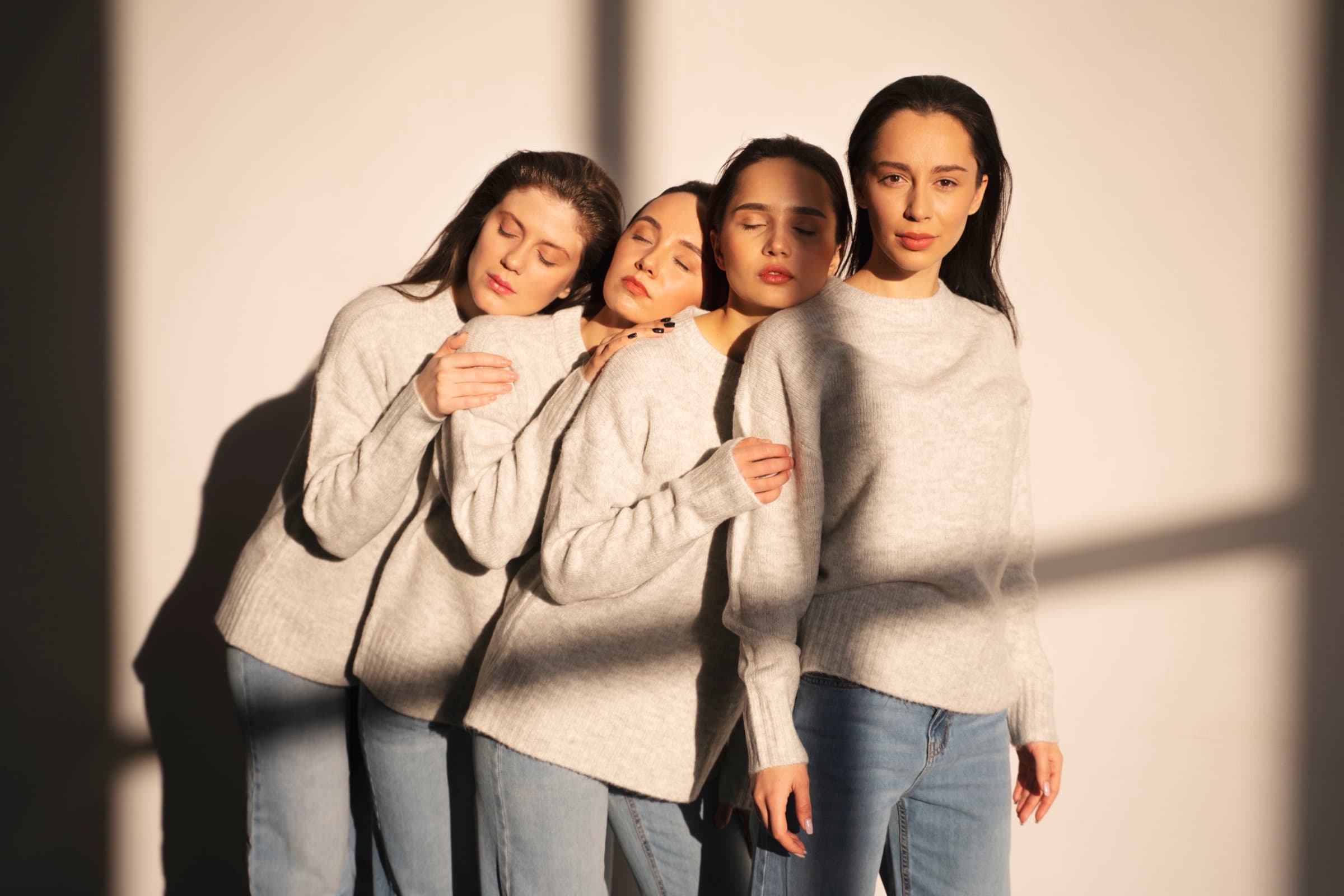 Four models in soft grey knitwear leaning together in warm window light — a Bespoke Beauty editorial portrait.