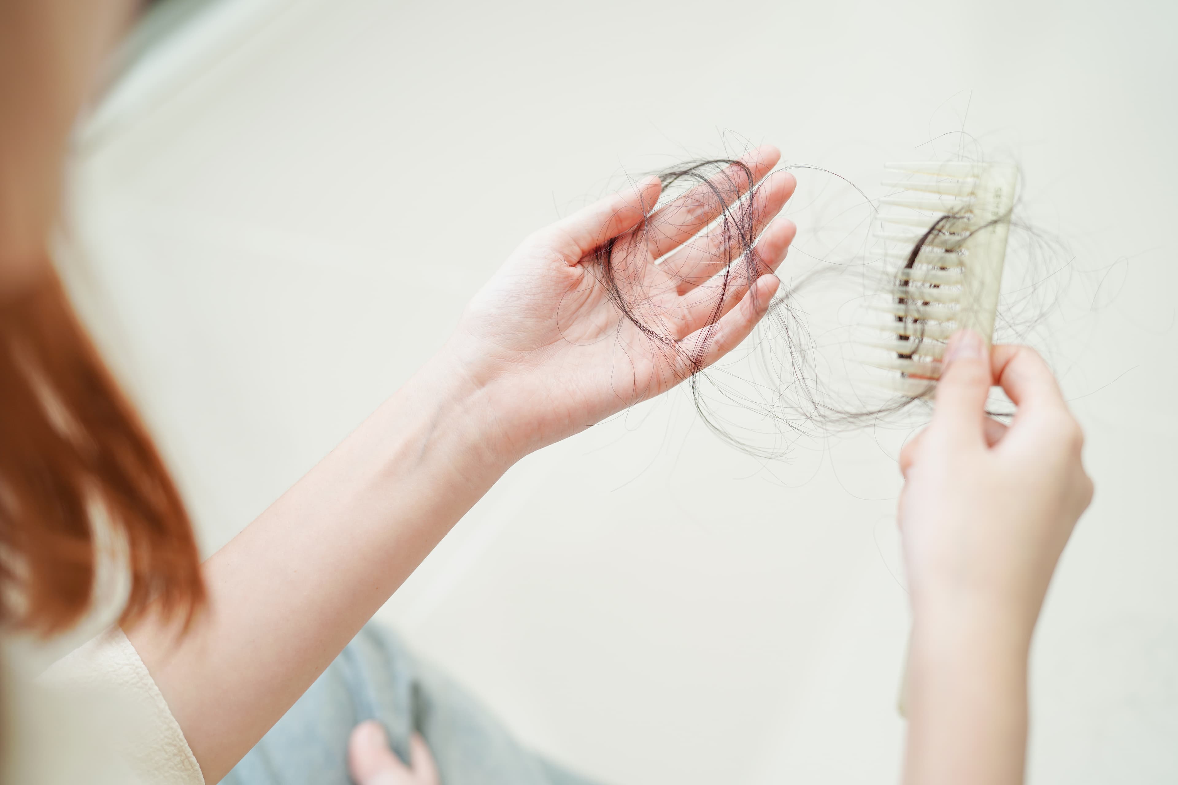 Sepasang tangan memegang sikat rambut dengan helai-helai yang tersangkut, momen jujur menghadapi kerontokan
