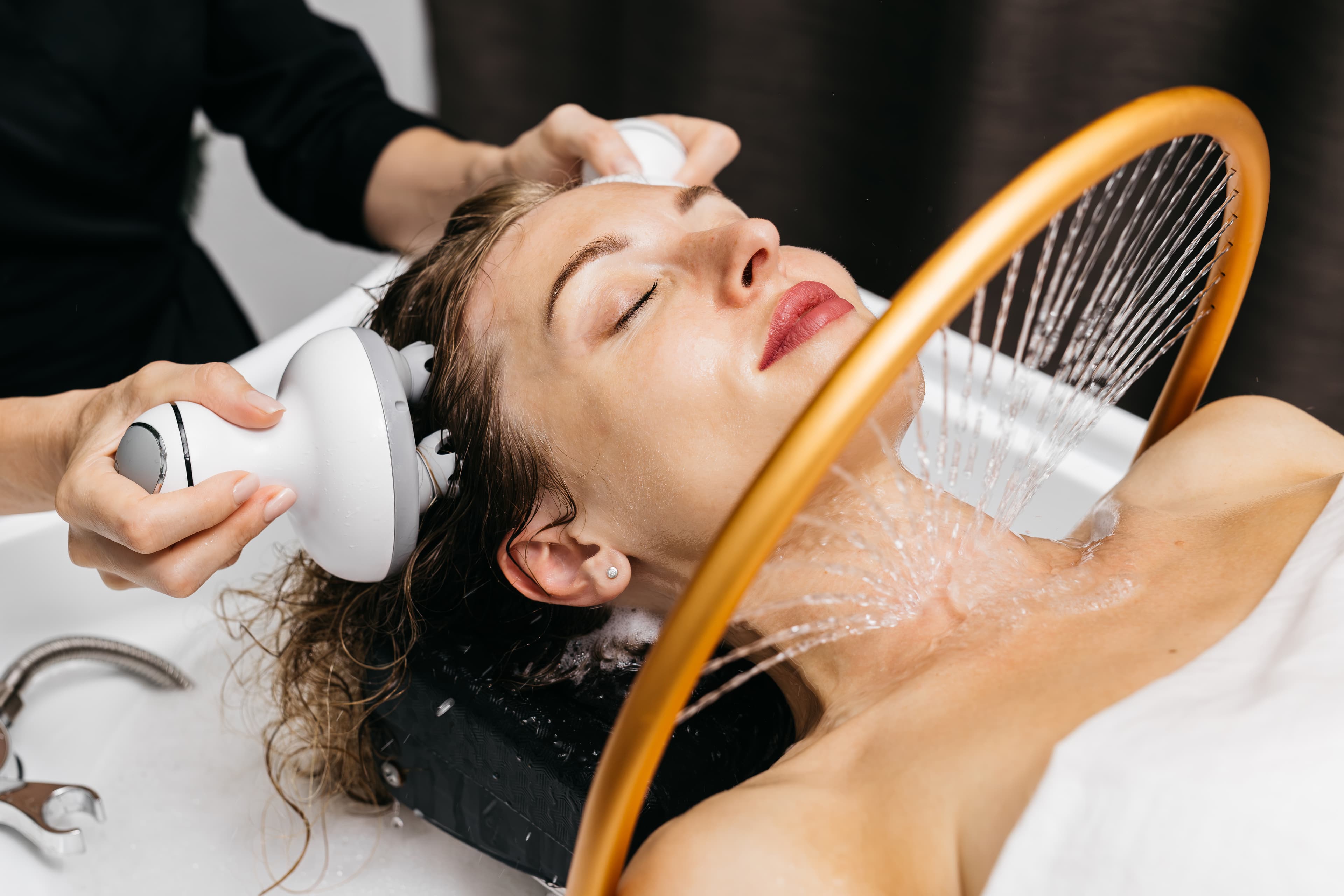 Seorang perempuan menerima perawatan rambut dan kulit kepala dari hairstylist di salon