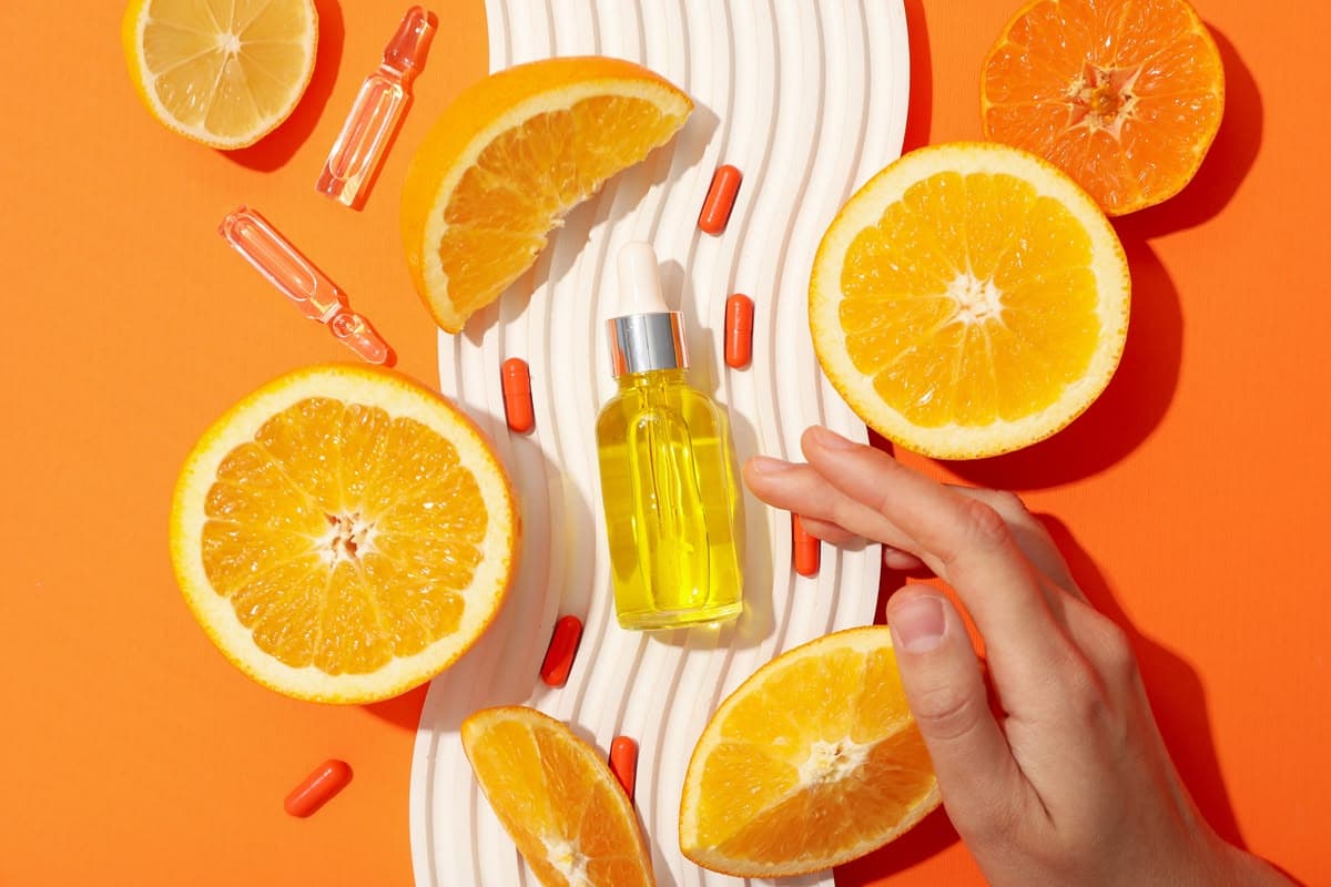 Tumpukan buah jeruk segar di samping tabung serum vitamin C berwarna cerah